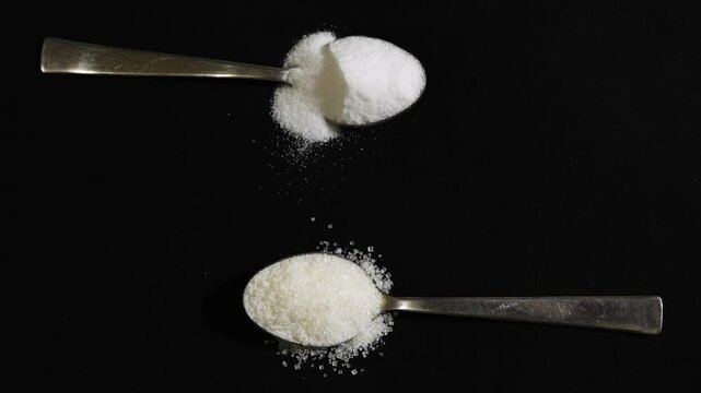 kitchen ingredient concept with sugar and salt on separate spoons
