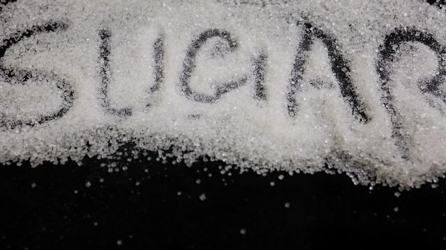 sugar word revealed through granulated sugar crystals on black background concept