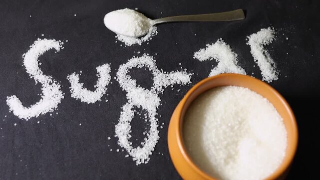 sugar text made from granulated sugar crystals with bowl and spoon on black background