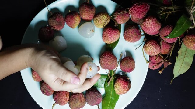 hands holding peeled lychee fruits with fresh lychee harvest on plate