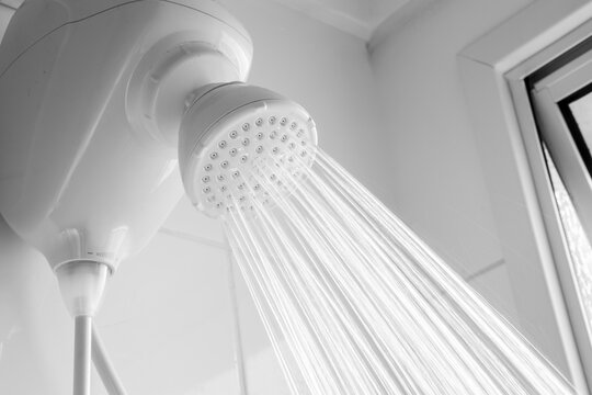 Close-up of a white electric shower head with strong water jets flowing in a modern bathroom interior. 