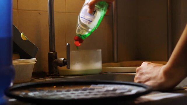 Hand of person washing dishes and utensils with soap and water on the sink.