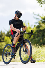 Fototapeta premium Cyclist checking his phone while riding on a road surrounded by trees on a sunny day during afternoon hours