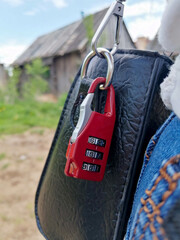 red combination lock with three digits is fixed on the carabiner of a black leather bag close up