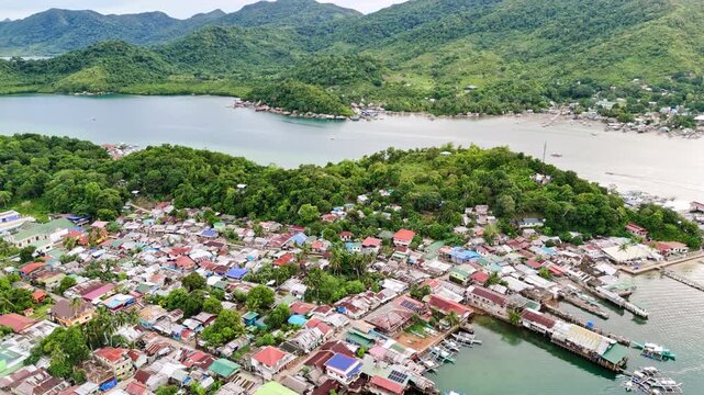 Pull-away aerial shot of creekside shanty houses in a coastal village in the Philippines. The drone reveals makeshift homes on stilts with rusty roofs lining the shore, capturing the reality of life