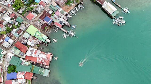 Push-in Bird-eye view shot over a coastal shanty town in the Philippines. The drone captures homes on stilts and small fishing boats scattered along the shore, offering a raw look at a seaside