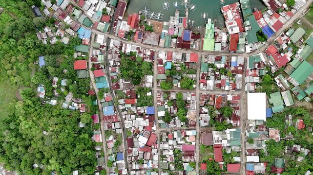 Push-in Bird-eye view from high altitude over a coastal shanty town in the Philippines. The aerial footage reveals creekside houses, stilt homes, and small boats along the ocean shore