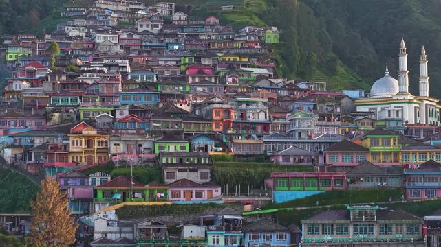 Aerial view of Peaceful village at the foot of green mountains with mosque and colorful houses. Beautiful rural landscape captured in soft natural lighting. Nepal Van Java, Indonesia.