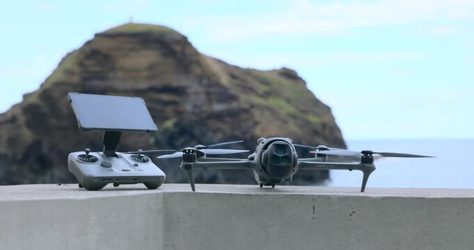 Drone and remote controller resting on a concrete surface with sea and cliff in background