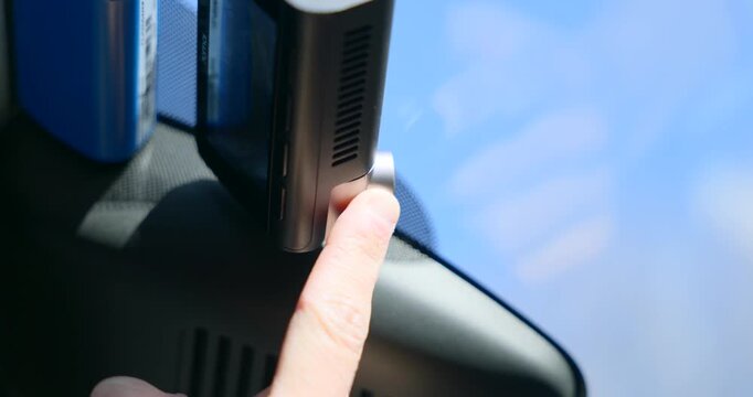 Hand adjusting a car dashcam mounted on the windshield, ensuring proper view for road safety