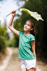 Naklejka premium Young girl holding a large leaf outdoors while enjoying nature in a summer setting