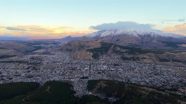 Esquel with snow covered mountains at sunset in Chubut, drone panoramic establishing backdrop from mountains to town below