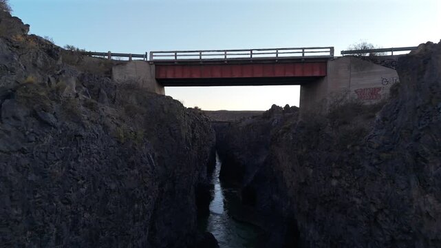 Volcanic canyon carved by the R&iacute;o Grande in La Payunia near RN40 and Pay&uacute;n Matr&uacute; volcanic region, Mendoza, Argentina, featuring basalt rock walls and bridge infrastructure, FPV forward flythrough shot