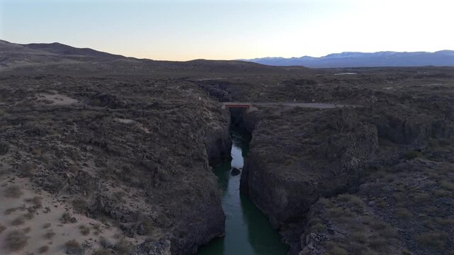 Stunning aerial footage flying over a deep river canyon carved through ancient volcanic rock in La Payunia Reserve, Mendoza, Argentina. Sparse desert landscape