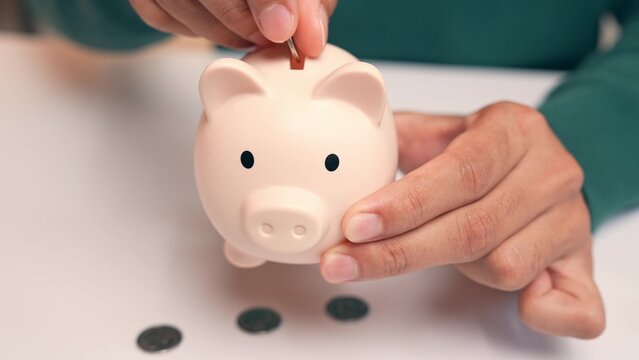 An office worker puts coins into a piggy bank, but they fall straight out the bottom, symbolizing failed saving efforts, financial setbacks, instability, and the frustration of unmet financial goals.

