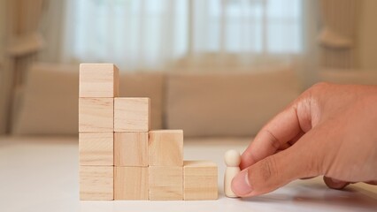 A wooden figure stands at the base of descending block steps, symbolizing stagnation, career decline, lost momentum, challenges in progress, resilience, and the importance of adapting to change.  © Punyawee