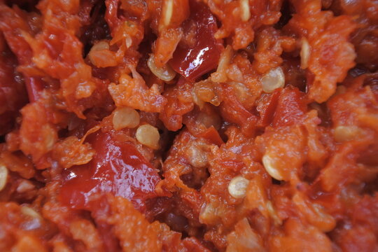Close-up abstract background texture of spicy red hot chili sauce paste with visible chili seeds and crushed peppers.