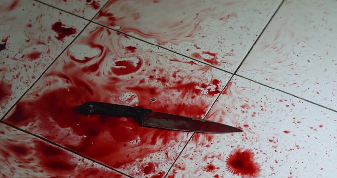 Slow motion shot of a bloody knife falling on the tile floor.
