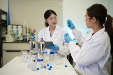 Fototapeta premium Two Asian Female Scientists Working Together in Modern Laboratory with Pipettes and Test Tubes