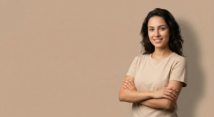 Obraz premium Portrait of a confident smiling young woman with folded arms wearing a casual t-shirt against a plain beige background with copy space