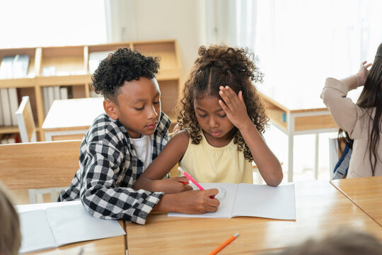 Kind boy helping classmate with homework in modern elementary classroom, Supportive students collaborating on school project, Friendly children learning together and studying at school desk