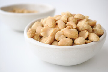 Fototapeta premium Bowl filled with shelled peanuts on a white background
