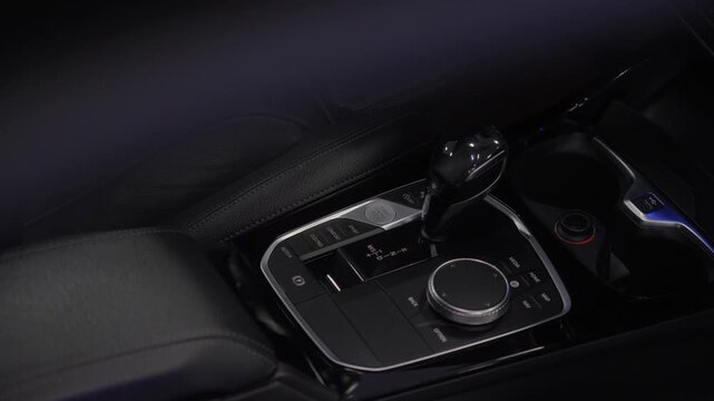 Car center console with automatic gear shifter, rotary controller dial and electronic brake button. Premium automotive cockpit detail.