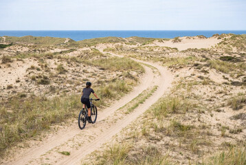 Fototapeta premium Female eMTB Rider Following Coastal Dune‑Side Path