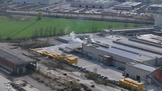 Drone descending over the Xella Ytong construction blocks factory in Pontenure, Piacenza, Italy, revealing warehouses, yellow block stacks, smoke chimneys and surrounding fields.