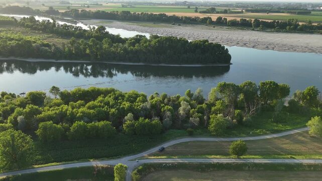 Aerial drone panning reveal over Po and Arda rivers junction at Isola Serafini, regional border between Emilia Romagna and Lombardy, green farmland, trees and Cremona skyline in background, Italy.