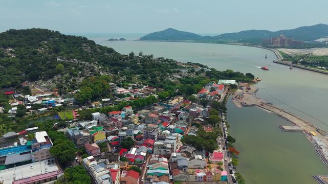Aerial parallax view over Coloane Village in Macau showing colorful rooftops, forested hillside, waterfront promenade and calm sea with distant islands