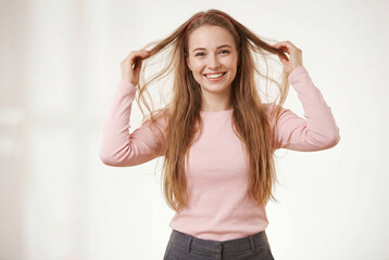 Naklejka premium Joyful young woman wearing a pink top playing with her long brown hair while smiling warmly