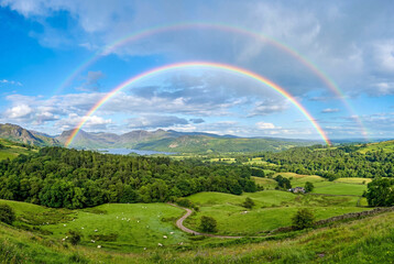 Fototapeta premium Large double rainbow arching over a green valley with a distant lake and mountain range