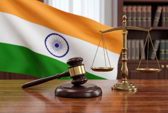 Wooden gavel and brass scales of justice resting on a desk with the indian flag displayed behind
