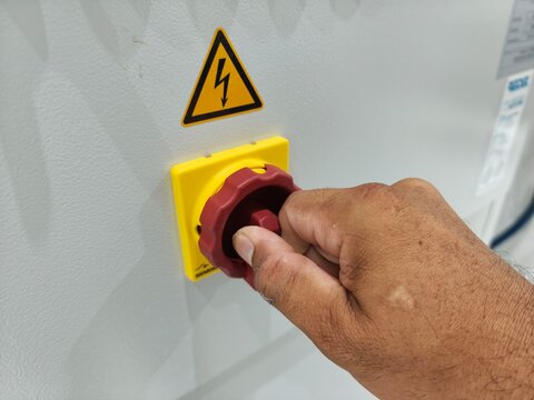 Close-up of worker bare hand turning main isolator switch on electrical panel