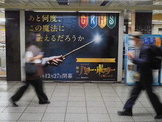Naklejka premium TOKYO, JAPAN - June 5, 2026: People pass a billboard in a subway station advertising the play Harry Potter and the Cursed Child. It notes that the production is going to close.