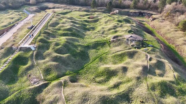 Low aerial view across grass-covered shell craters, paths, and woodland at historic Fort de Vaux near Verdun, France.