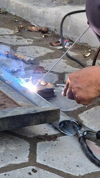Worker Welding Metal Hinge Bracket on Heavily Rusted Iron Gate Frame Using Stick Welder