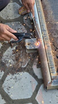 Worker Welding Metal Hinge Bracket on Heavily Rusted Iron Gate Frame Using Stick Welder