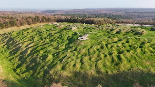 Aerial landscape of Fort Douaumont with rolling grass mounds, historic fort structures, and surrounding forest near Verdun, France.