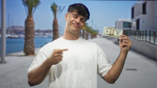 Man holding dollar and points finger at it on street, hand raised in smirk gesture; bravado confidence.
