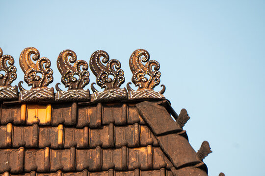 Traditional Javanese roof, specifically known as a wuwungan, is characterized by intricate, hand-made clay tiles, often decorated with detailed tendril or scroll motifs.