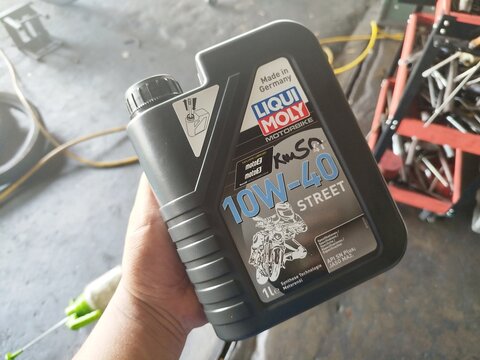 KUALA TERENGGANU MALAYSIA- JUNE 09. 2026.. A close-up of a person's hand holding a 1-litre black plastic bottle of Liqui Moly Motorbike 10W-40 Street engine oil inside a mechanical workshop.