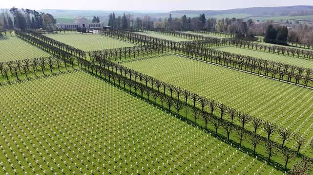 Drone view of white grave crosses in orderly rows on green lawn at Meuse-Argonne American Cemetery and Memorial in France.