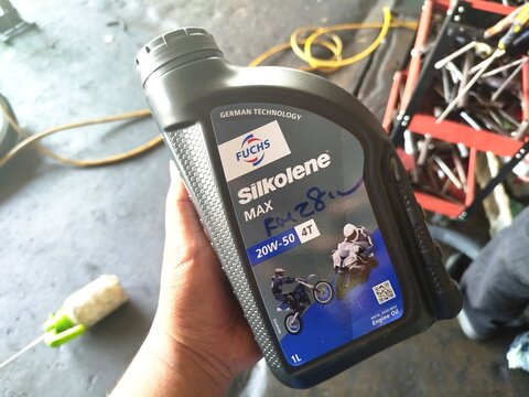 KUALA TERENGGANU MALAYSIA- JUNE 09. 2026.. A close-up of a person's hand holding a 1-litre bottle of Fuchs Silkolene Max 20W-50 4T motorcycle engine oil inside a repair workshop.