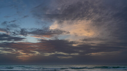 Fototapeta premium Evening after sunset, seascape. Purple clouds in the sky are colored with golden and scarlet. The waves of the turquoise ocean roll towards the shore. Twilight. Cuba. Varadero. 