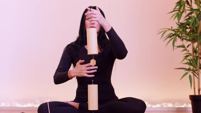 Spiritual concentration. Sound healing. Female doing ritual with bamboo wind chime instrument on meditation session in balance pose in studio.