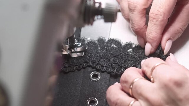 Seamstress occupation. Garment making. Female hand decorating black clothes with lace. Precision needle work on electric stitching machine.