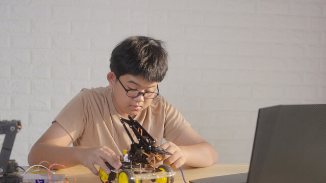Asian young student assembling a robotics car at home during STEM learning. Concept of coding education, engineering skills, innovation, and hands-on technology training.
