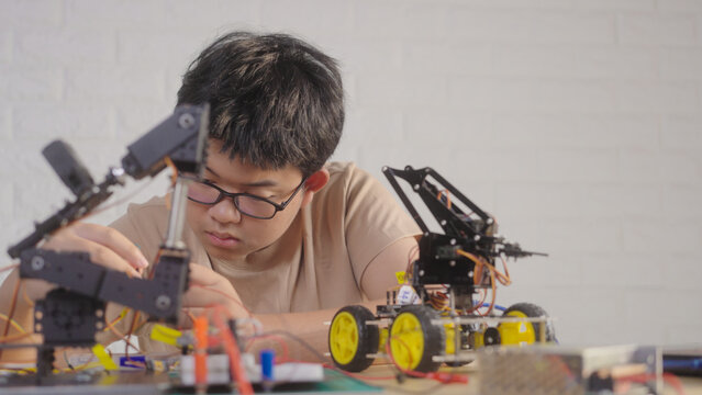 Asian young student building electronic circuits and a robotics project at home with robotic devices and a laptop. Concept of STEM education, engineering skills, and technology learning.